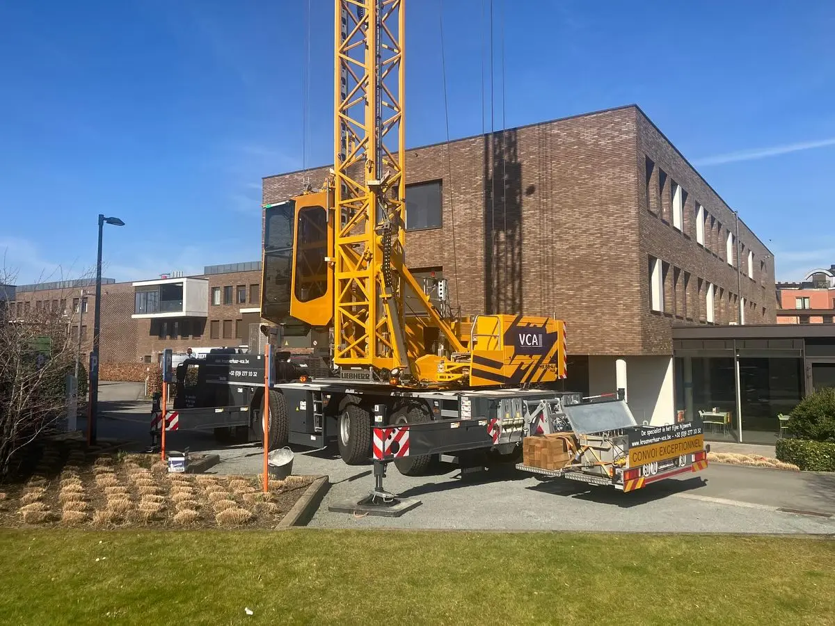 Mobiele torenkraan opgesteld naast een kantoorgebouw, giek verticaal in de lucht