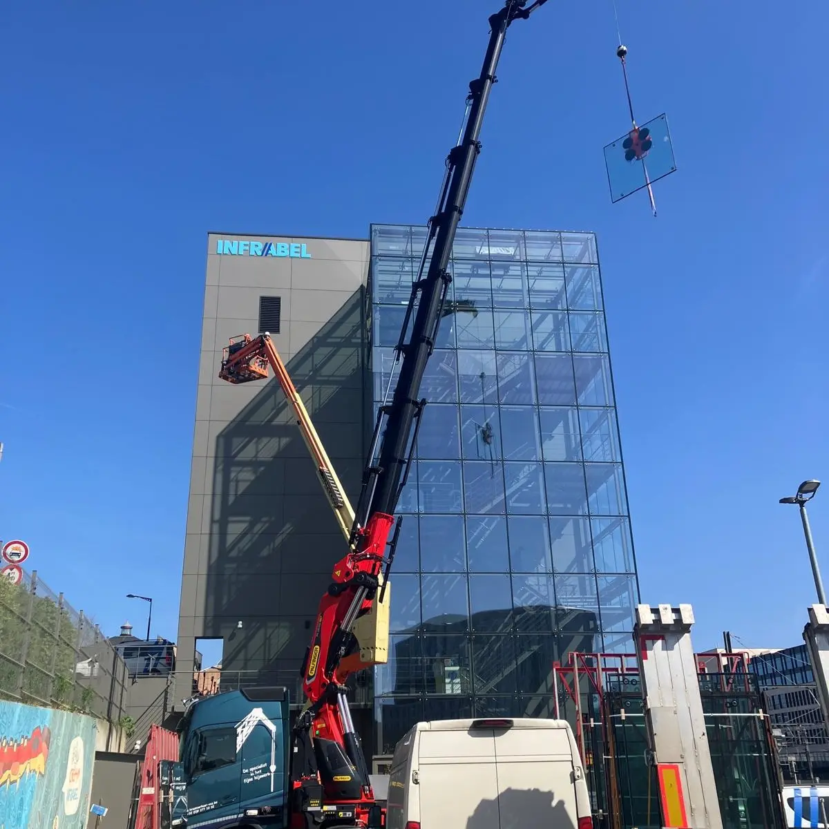 Palfinger PK 135 autolaadkraan hijst een glaspaneel langs een glazen gevel omhoog